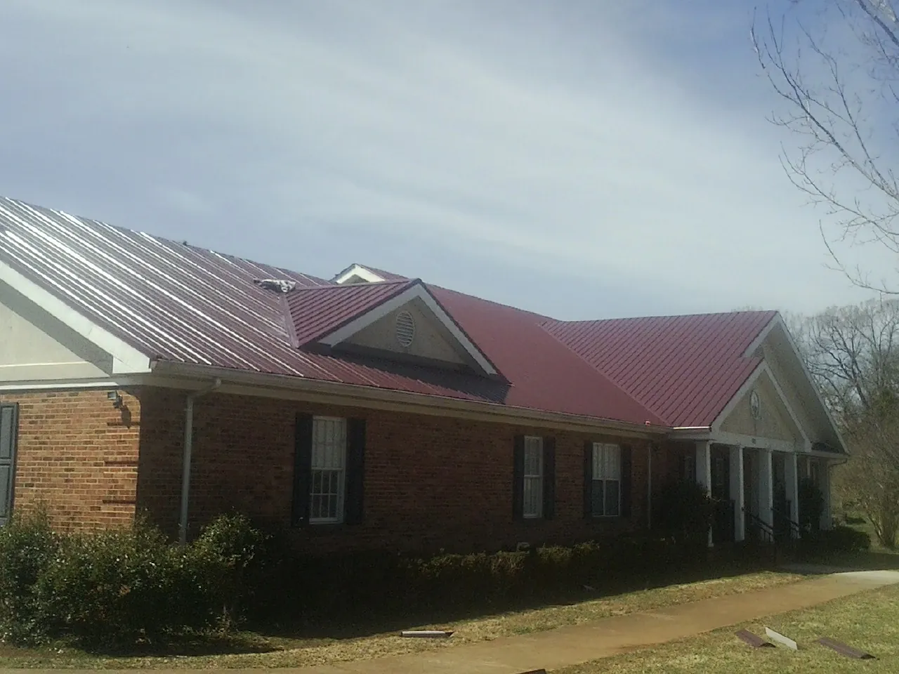 Red metal roof with gabled entries on a long brick building, from a Hail Damage Roof Repair job in Mill Valley