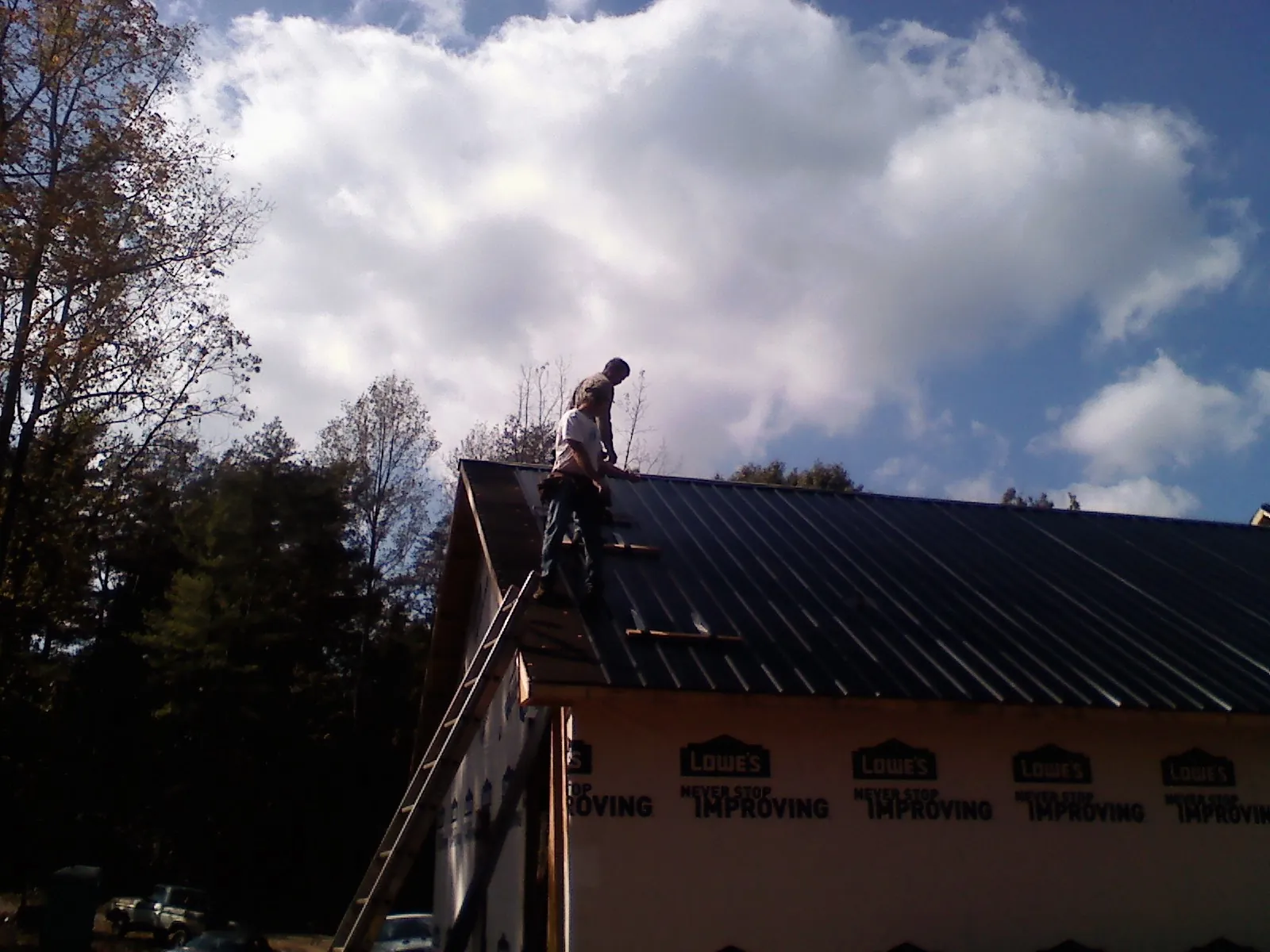 Roofer fastening dark metal panels high against a cloudy sky, from a Roof Inspection job in Mill Valley